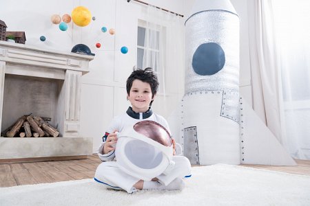 Chłopiec w stroju kosmonauty siedzi na dywanie w pokoju